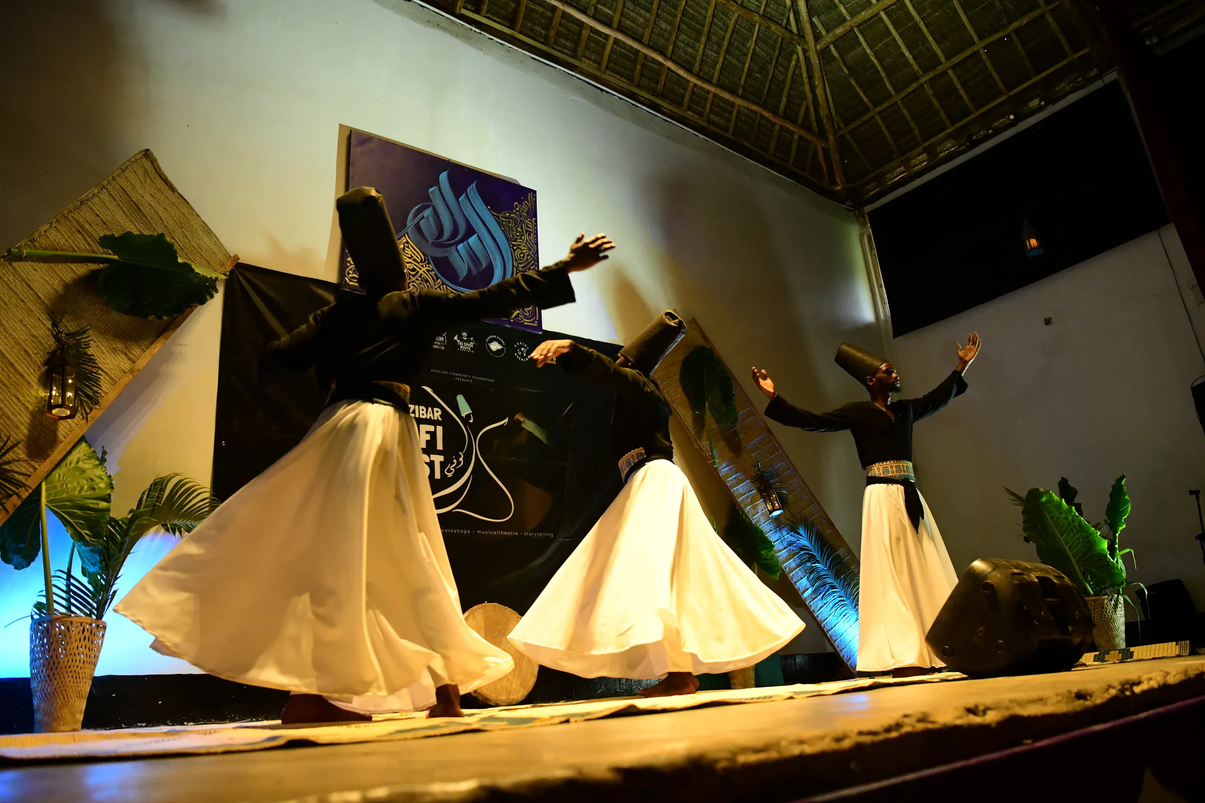 Three whirling dancers in tall hats and white skirts turning on a lantern-lit stage