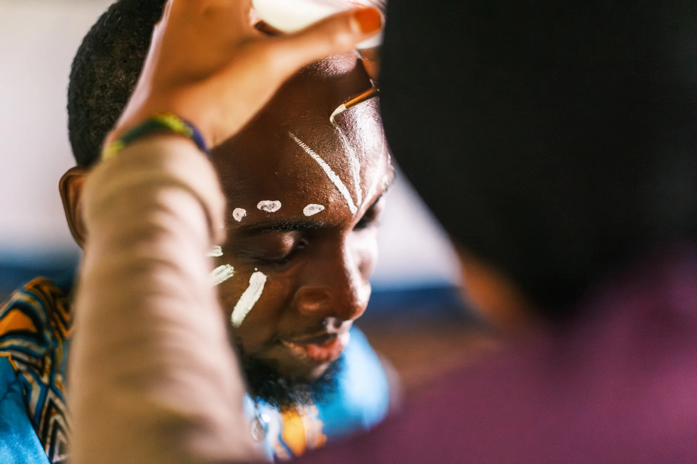 Close view of a brush laying a line of white paint across a performer's forehead backstage